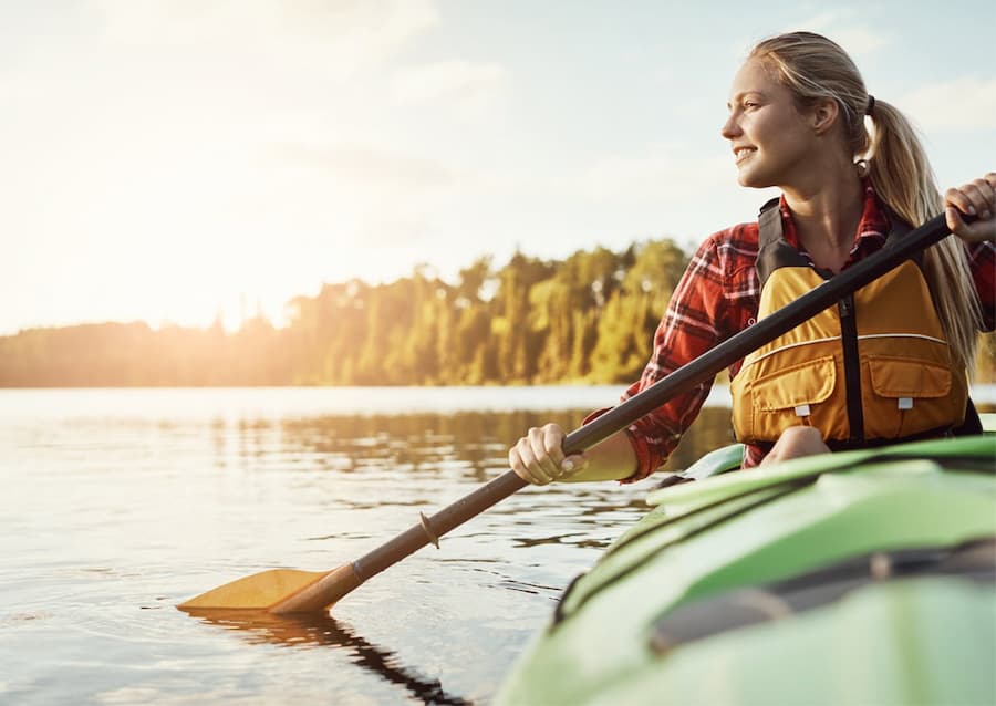 A person in a lifejacket smiles in a green kayak while paddling.