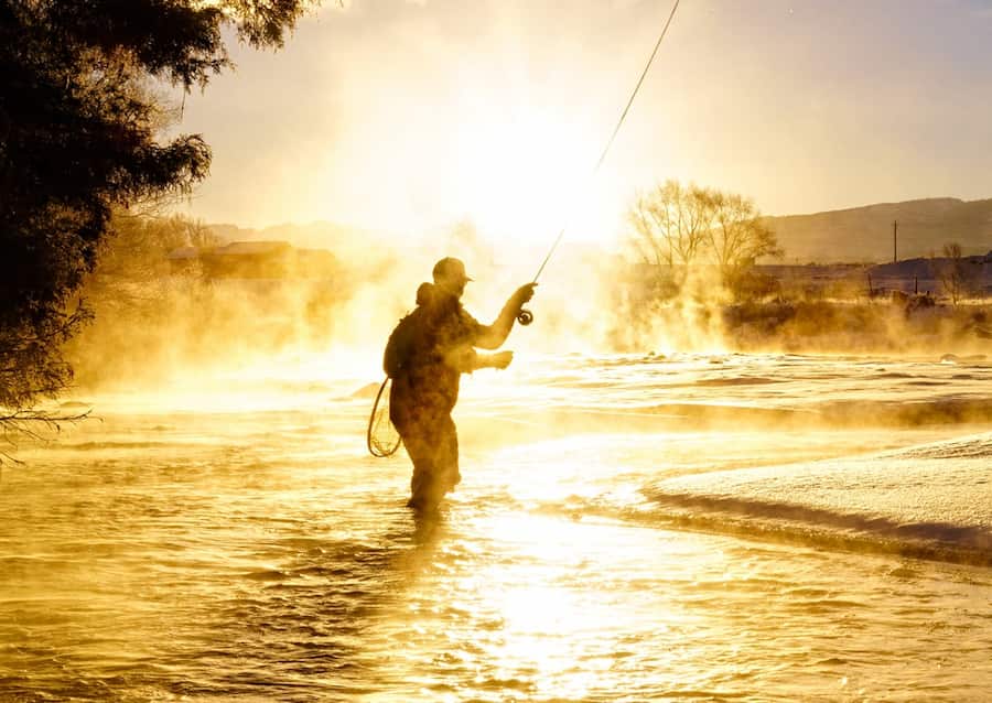 The silhouette of a fly fisher in the morning mist during sunrise.