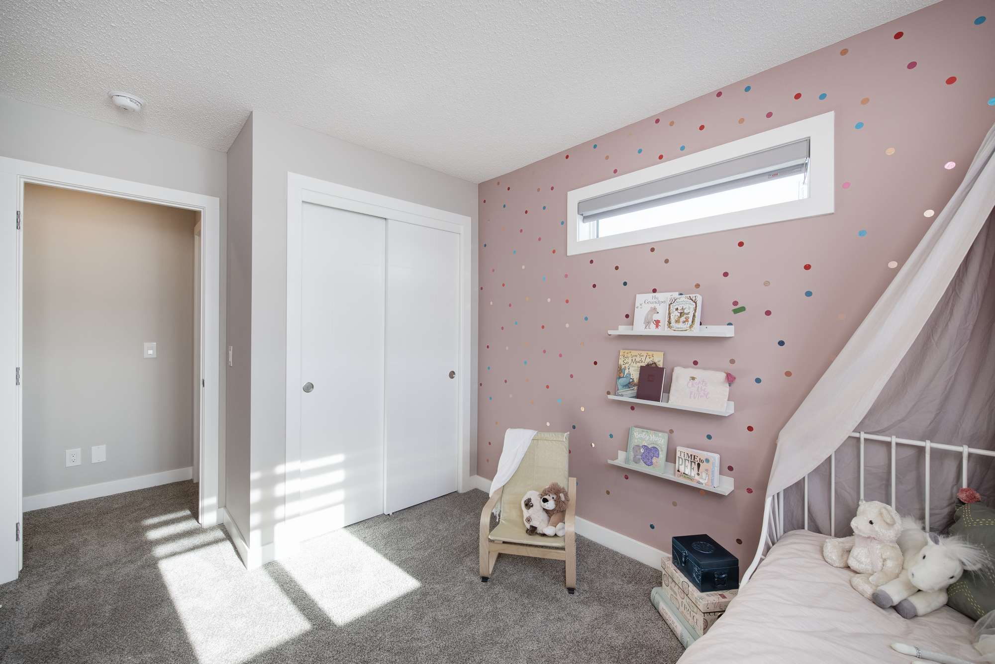 A child's bedroom with pink walls, stuffed animals, and a small chair.