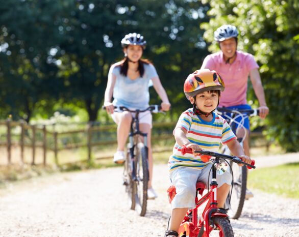 Two adults and a child ride their bikes on a gravel path through trees.