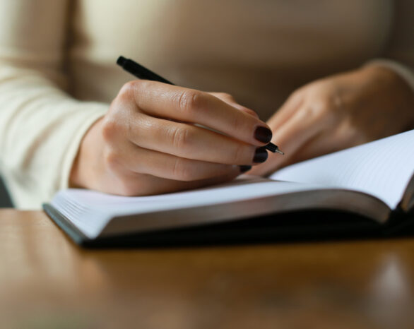 A person with black nail polish writes in a journal with a black pen.