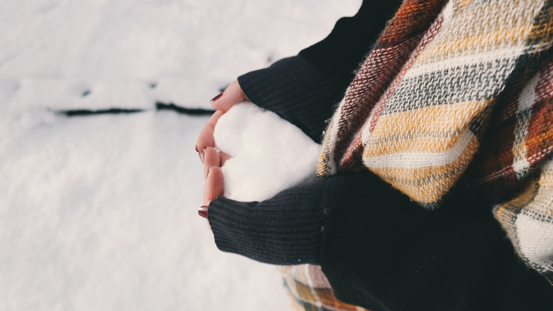 A person wearing a scarf holds a snowball shaped like a heart.