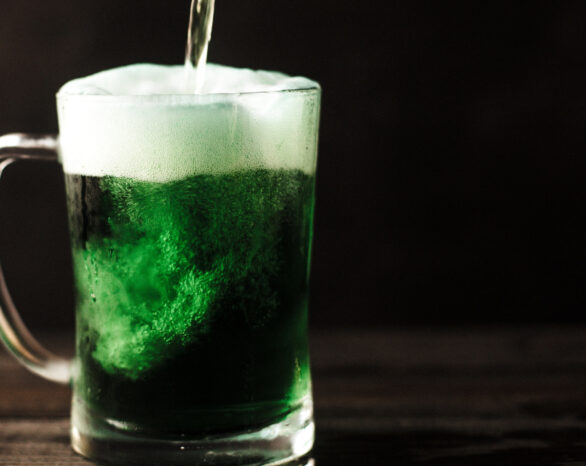 A pint glass with a handle is being filled with green beer.