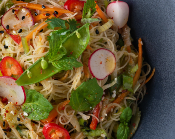 A noodle dish with radishes, peas, herbs, and carrots on a blue plate.