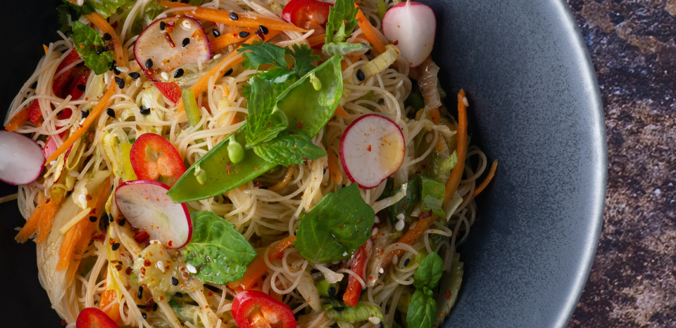 A noodle dish with radishes, peas, herbs, and carrots on a blue plate.