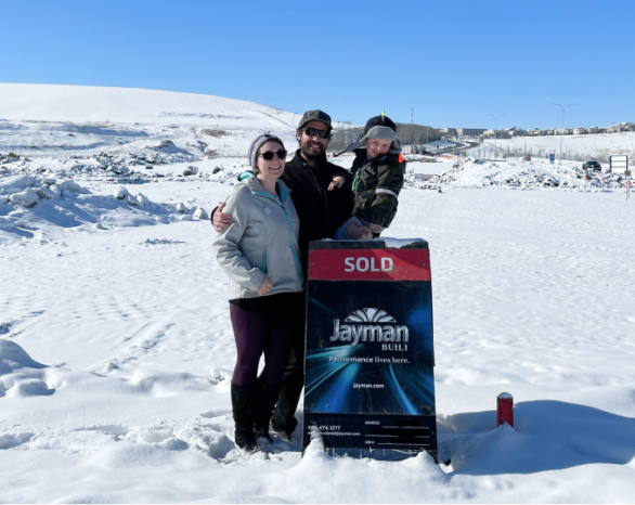 Two adults and a child stand behind a Jayman BUILT sold sign.