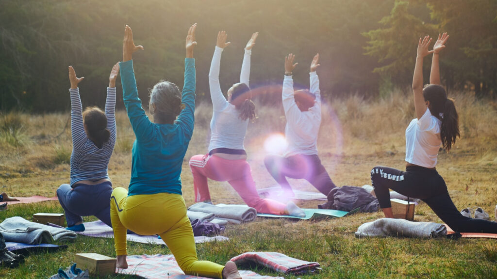 A group of five people doing yoga outside in a grassy area.