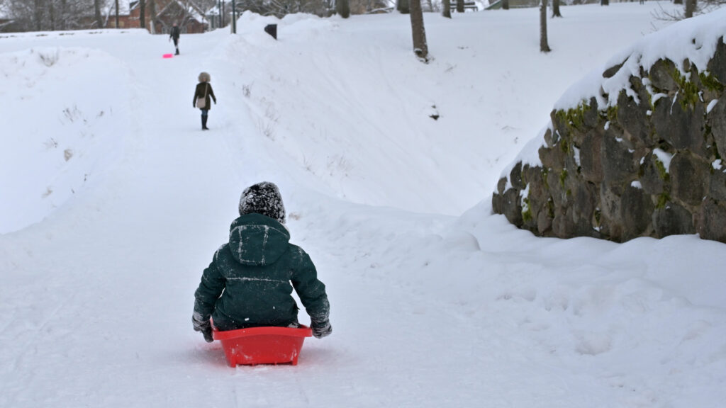 kid tobogganing down a hill in the snow