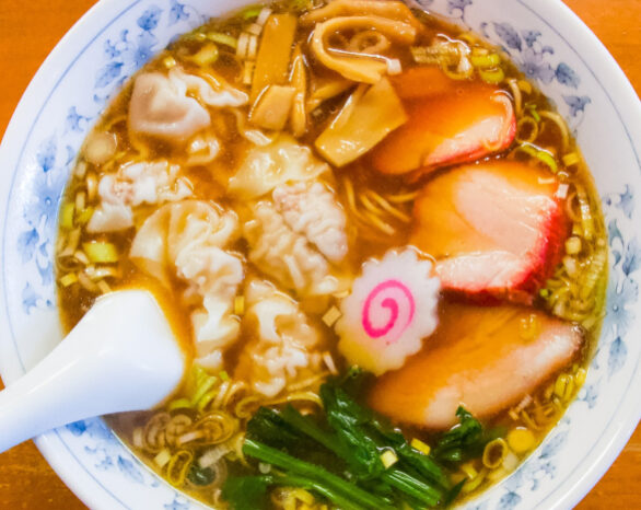 Soup with dumplings, fish cake, meat, noodles, and greens.