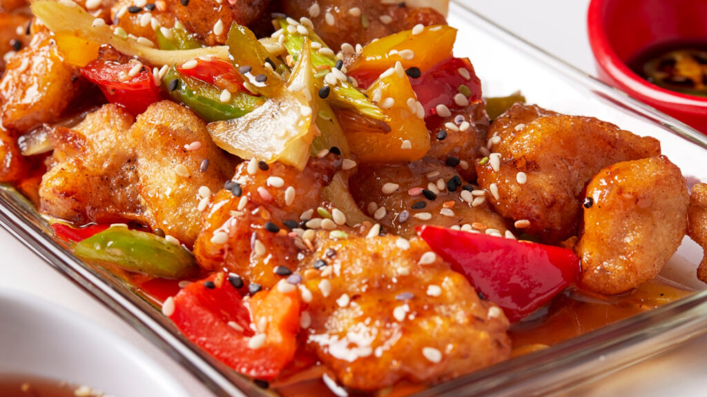 plate of orange chicken with red and green peppers and sesame seeds