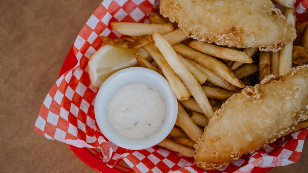 fish and chips with tartar sauce in a red basket with red and white checkered paper
