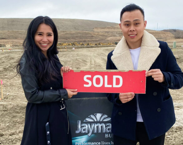 new homeowners stand outside next to a "sold" jayman built sign