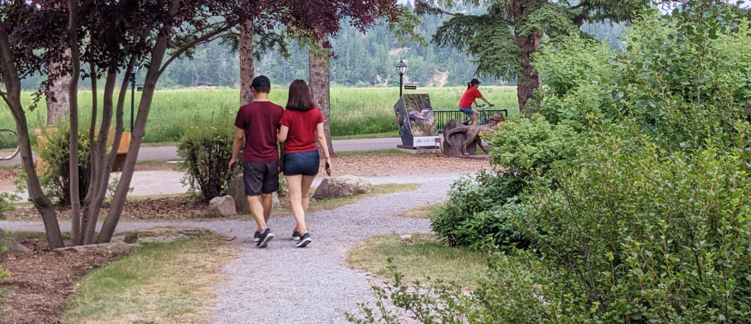 a couple wearing red shirts walking through fish creek park with a cyclist in the background