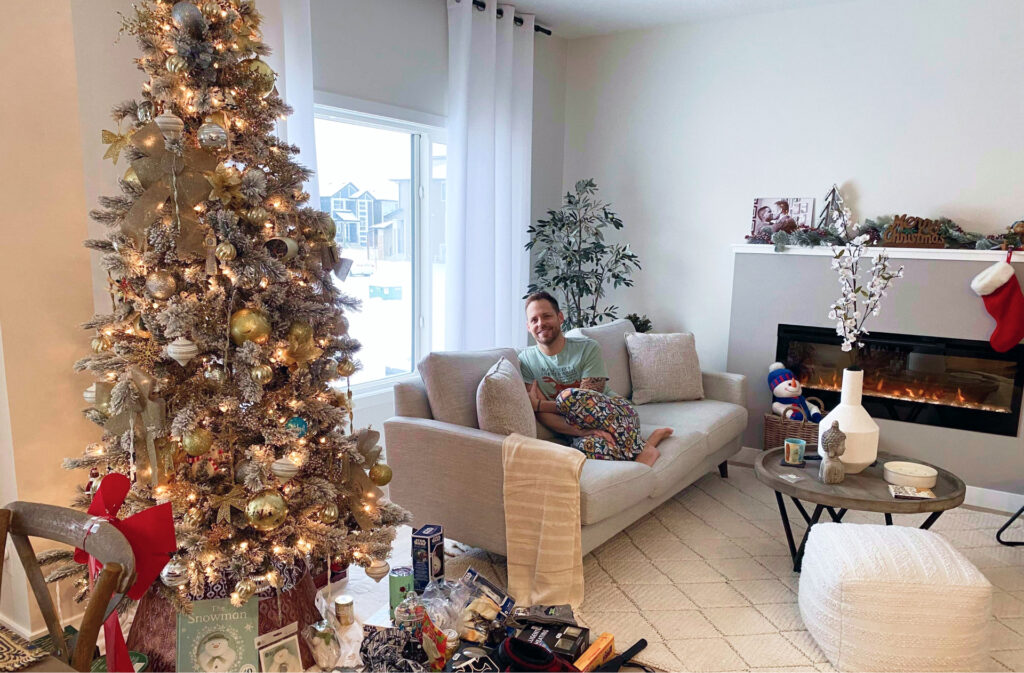 person sitting on a couch in a living room with a christmas tree and presents
