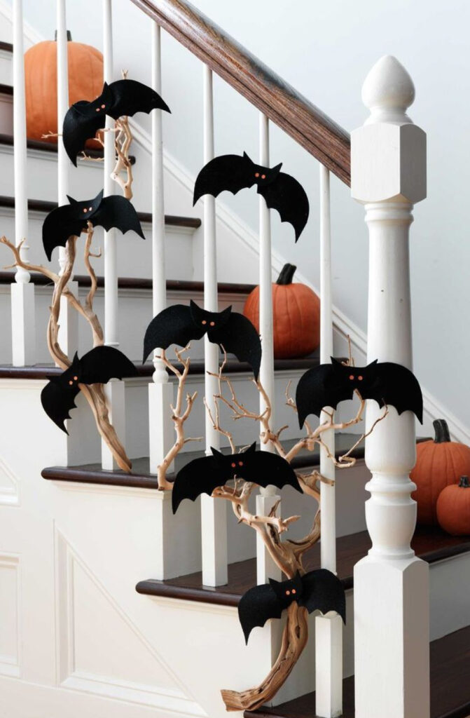 a staircase decorated with twigs, black paper bats and pumpkins